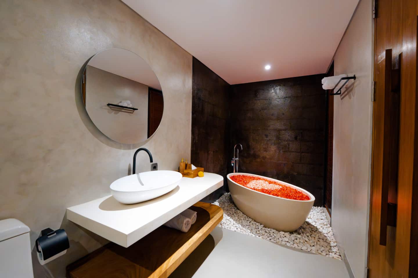 Freestanding bathtub filled with red flower petals beside a stone wall